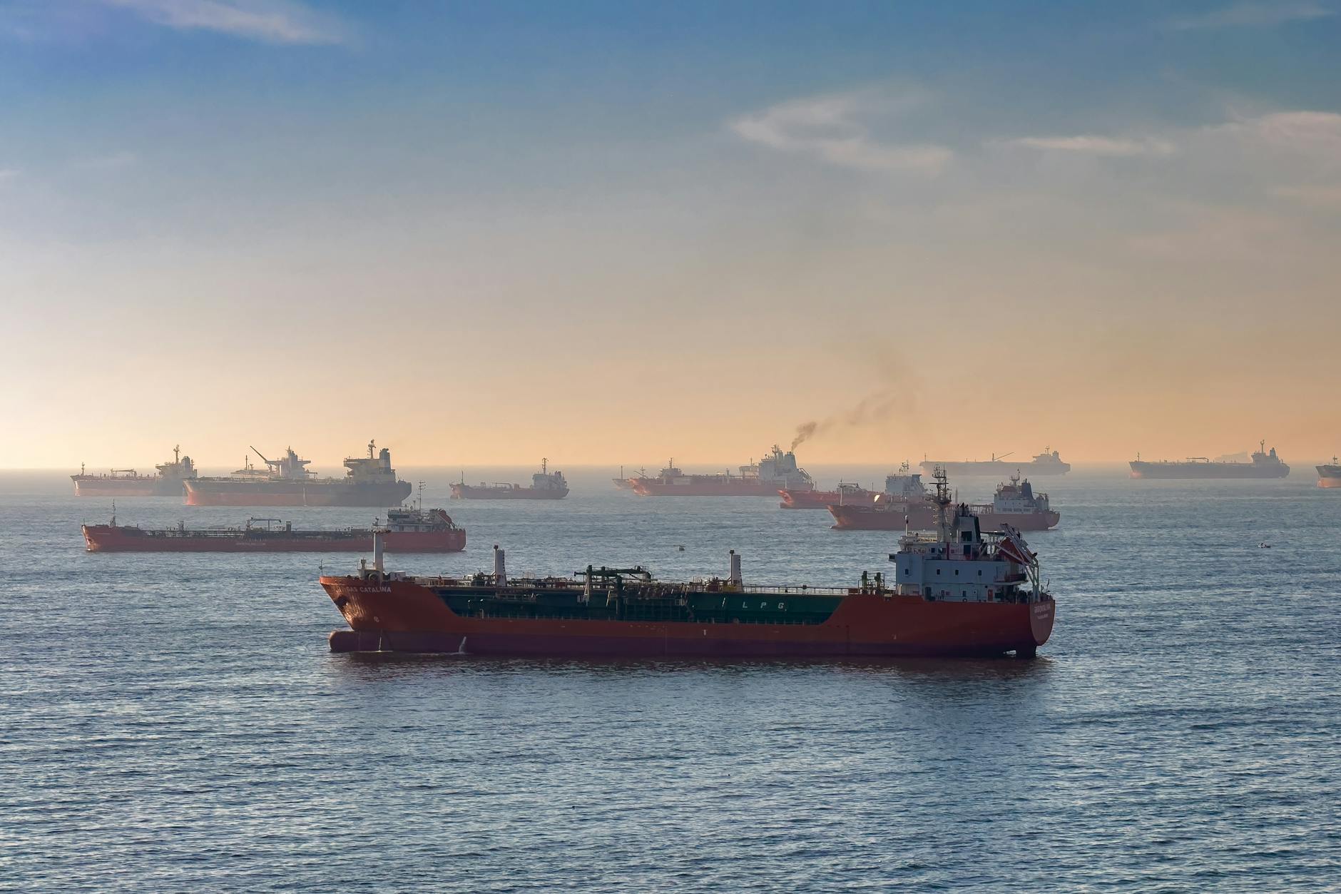 Oil tanker passing through the Strait of Hormuz with naval vessels in background